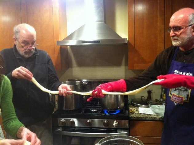 Two men stretching mozzarella in a kitchen